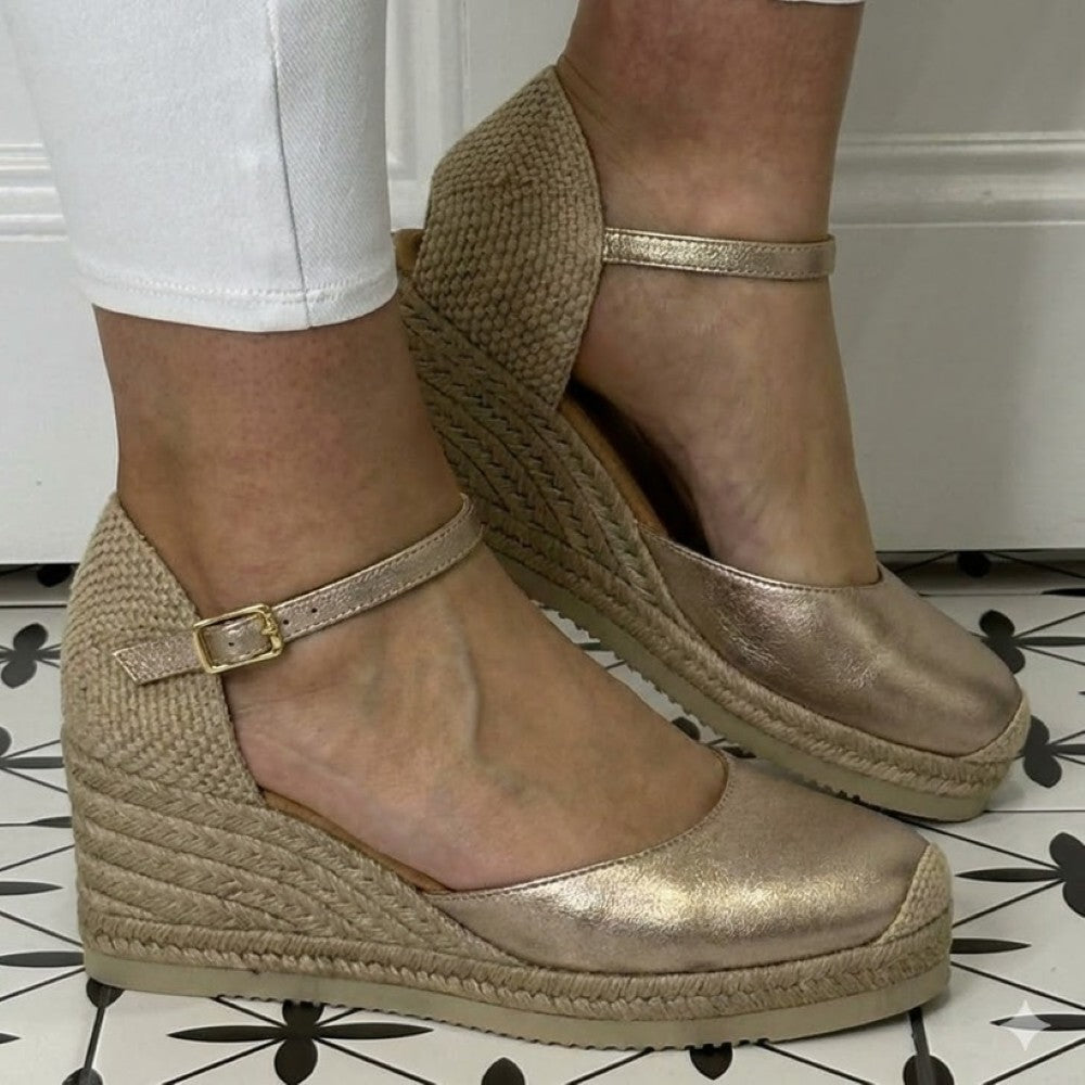 Unisa Caceres Gold wedge sandals with woven details worn indoors on a patterned floor.