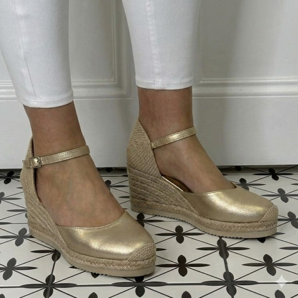Unisa Caceres Gold wedge sandals with woven details worn indoors on a patterned floor.