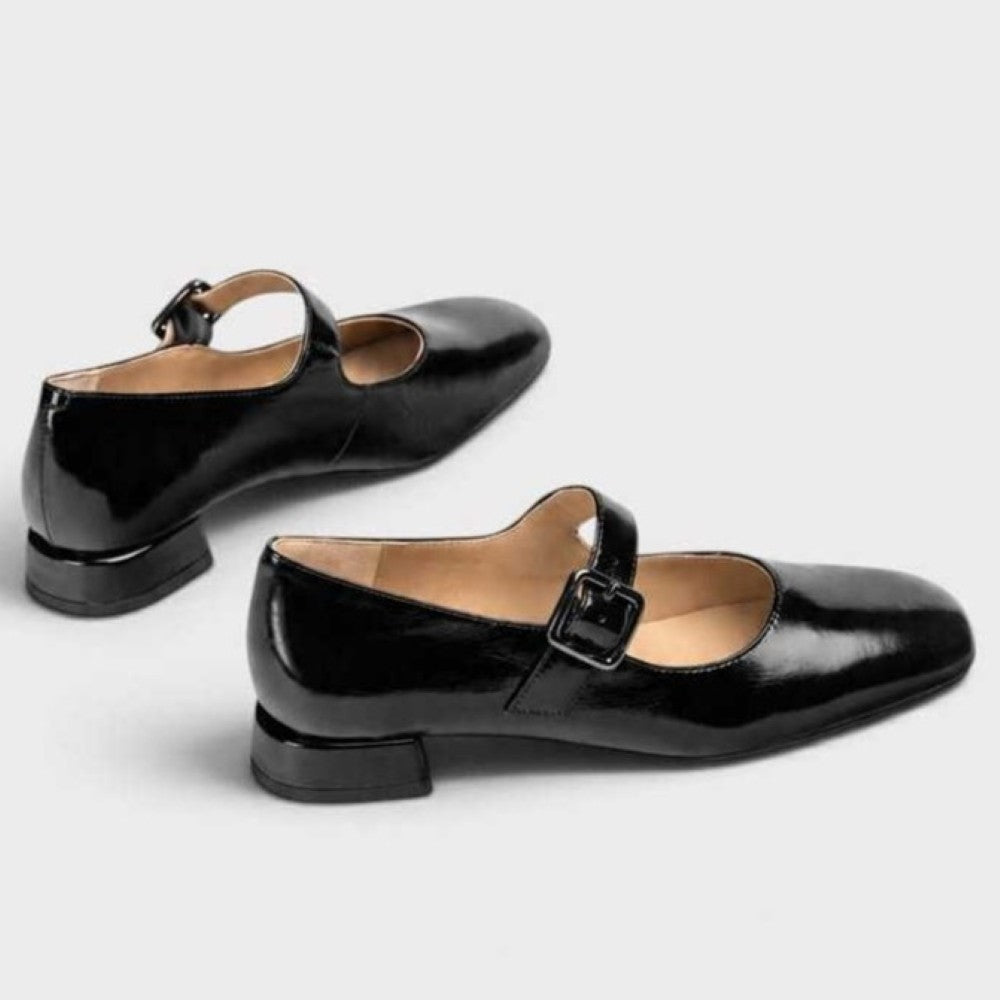 A pair of Unisa black patent leather Mary Jane shoes with low block heels and buckle straps, displayed on a light grey background.