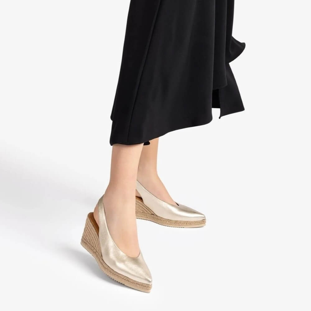 unisa Gold wedge sandals worn with black dress on a white background