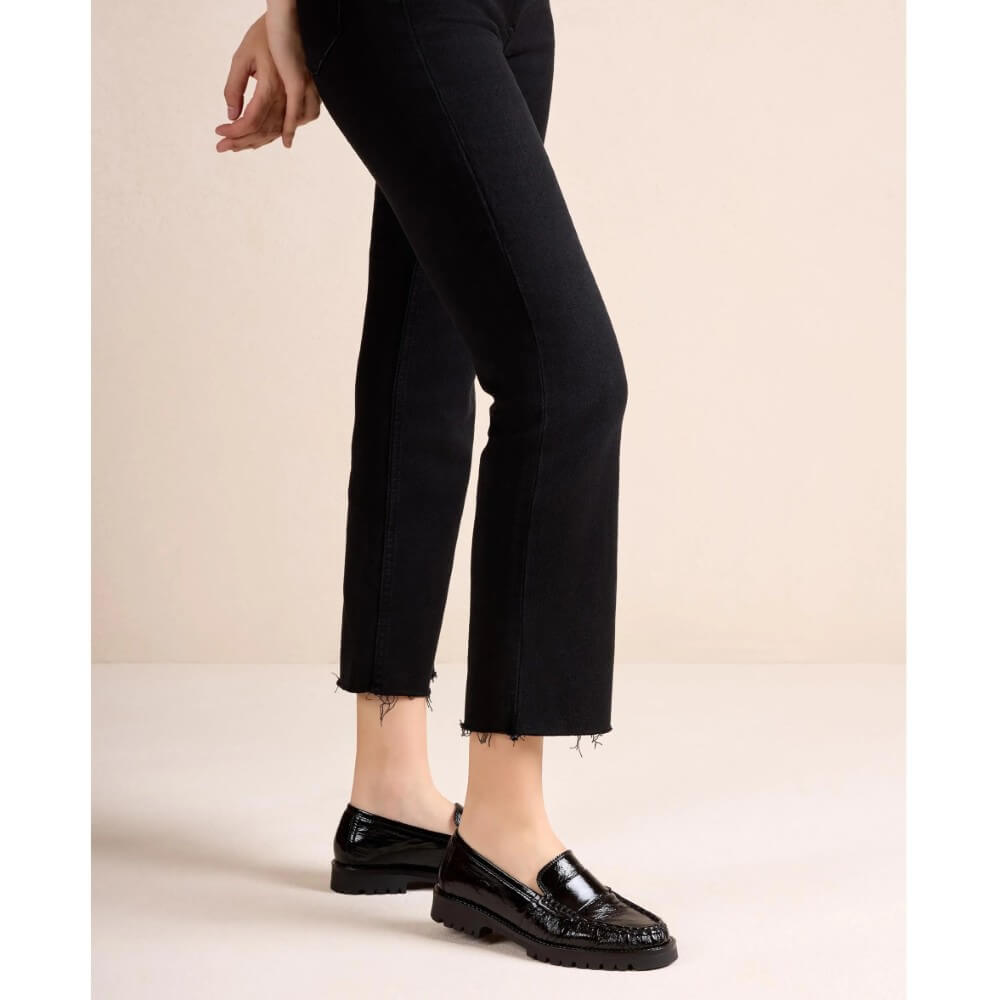 Black cropped ankle jeans with a raw frayed hem, shown on a model wearing  Unisa black patent leather loafers against a solid beige studio background.