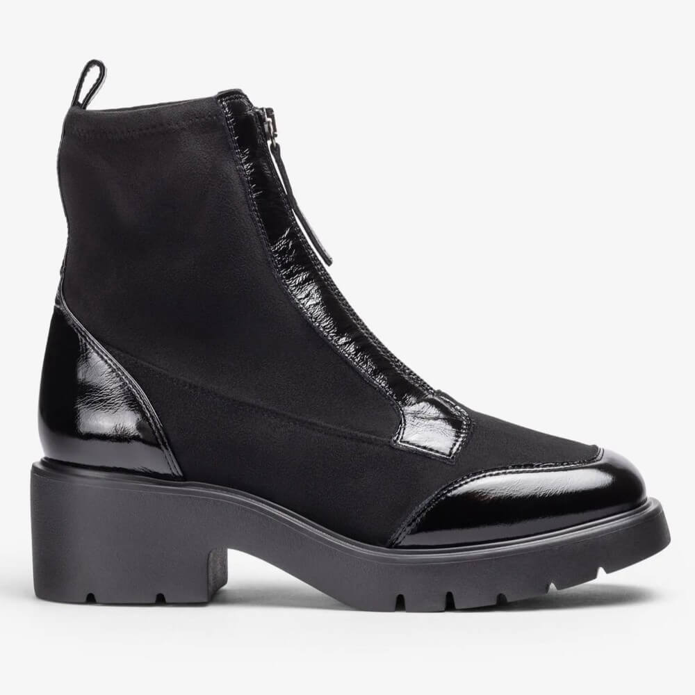 A Unisa black ankle boot with a chunky lug sole, patent leather toe cap, and front zipper, shown from a side profile on a light grey background.
