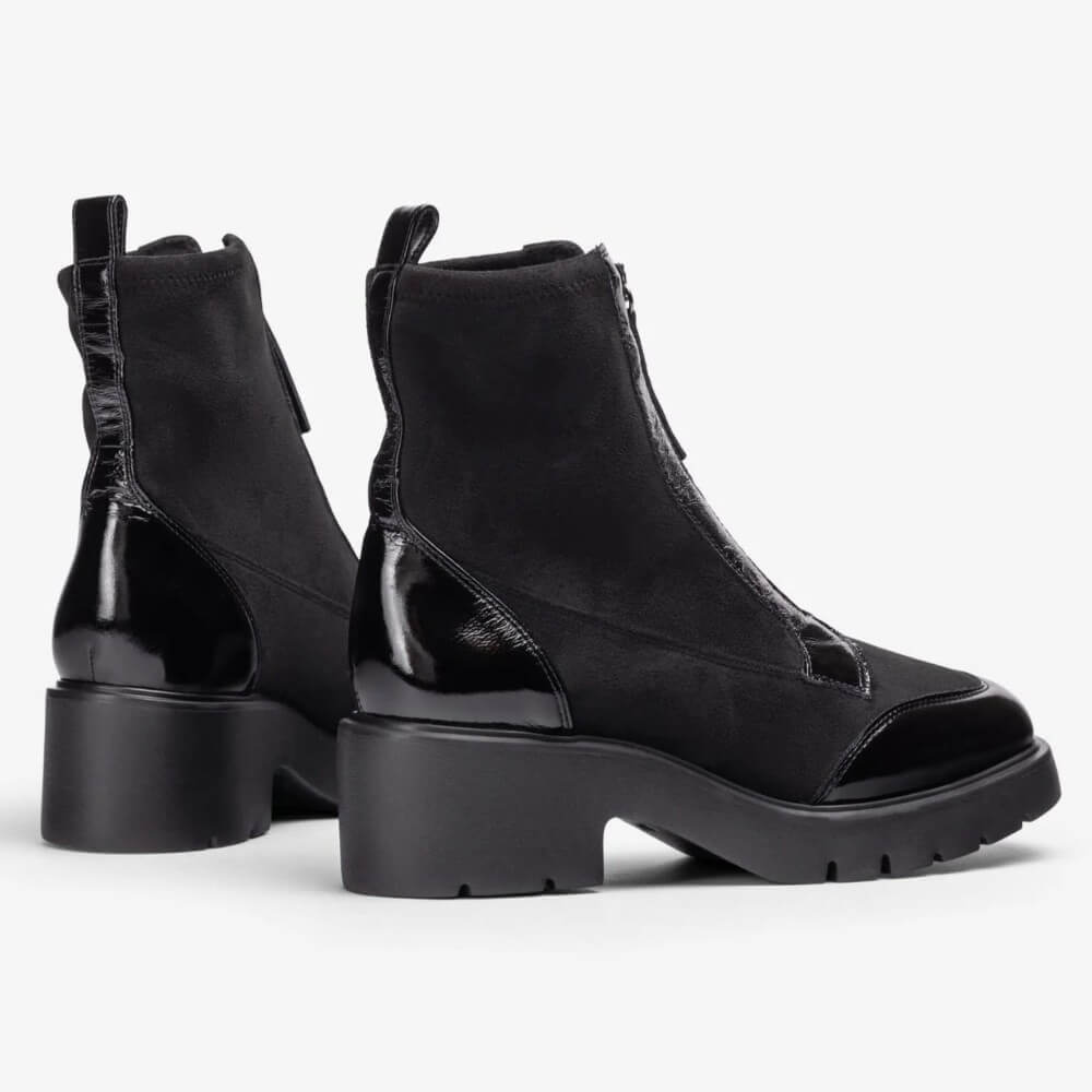 A pair of Unisa black ankle boots with a mix of matte suede and glossy patent leather panels, featuring chunky lug soles and a block heel, shown against a plain light grey background.