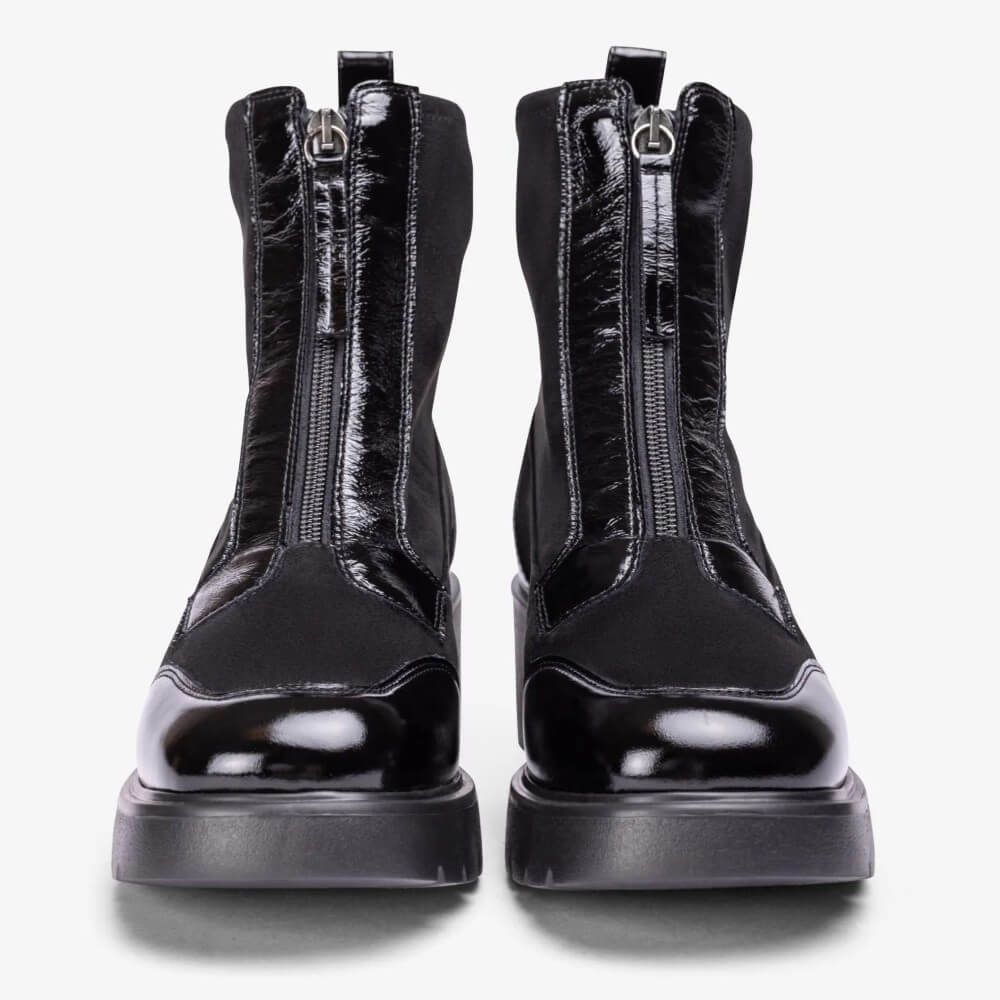 A Unisa black ankle boot with a chunky lug sole, patent leather toe cap, and side zipper, shown from a side profile on a light grey background.