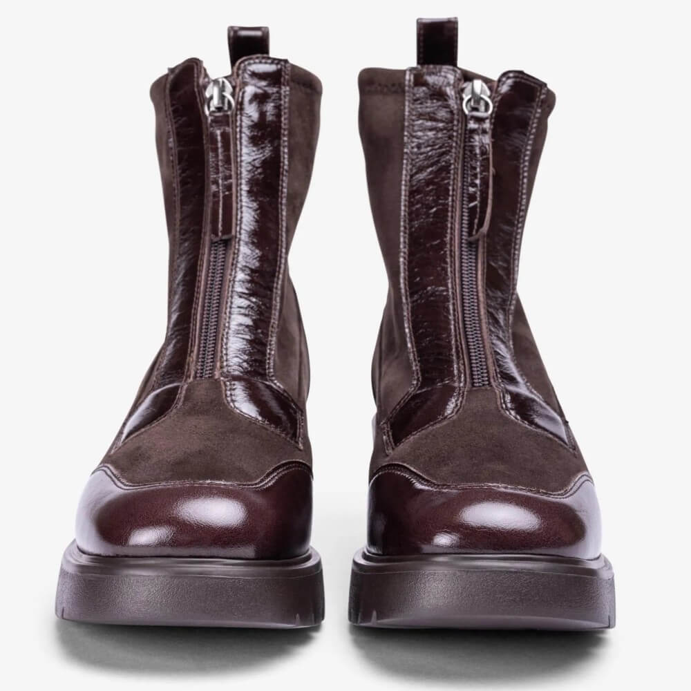 A pair of dark brown ankle boots with a mix of patent leather and suede panels, featuring front zippers and chunky soles, shown against a plain light grey background.