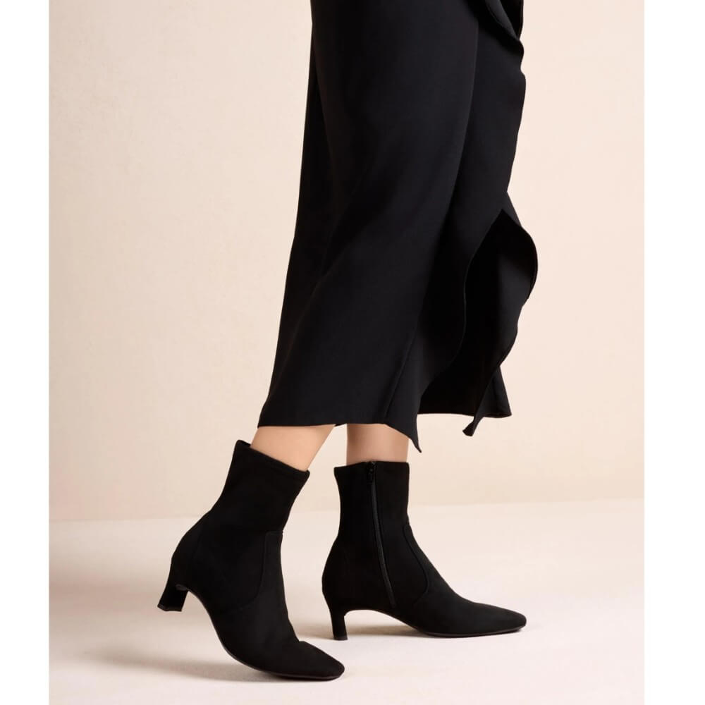 Person wearing a pair of Unisa Jarret Ankle Boot Stretch Black with a black dress