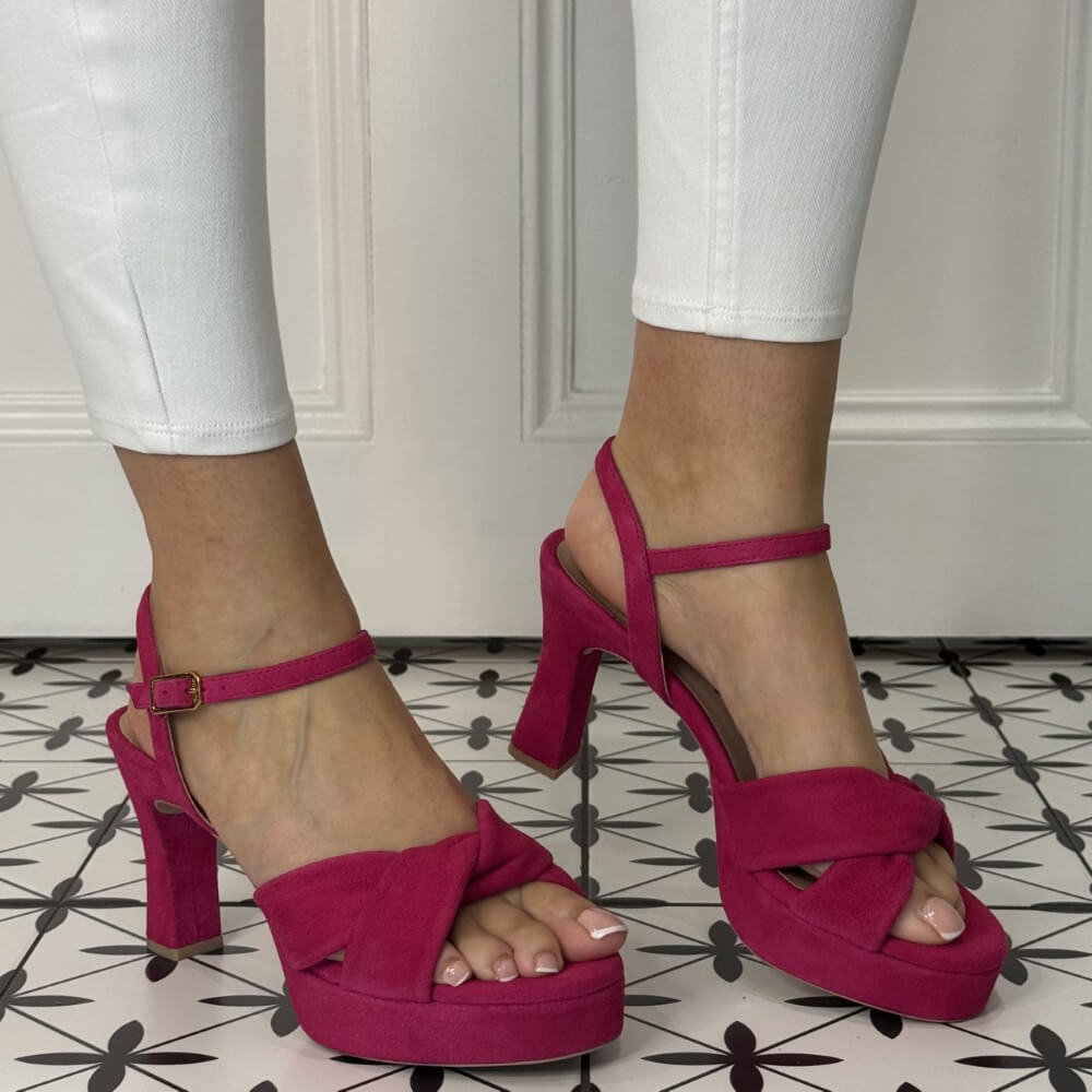 Pink high-heeled sandals worn with white pants on a patterned floor.