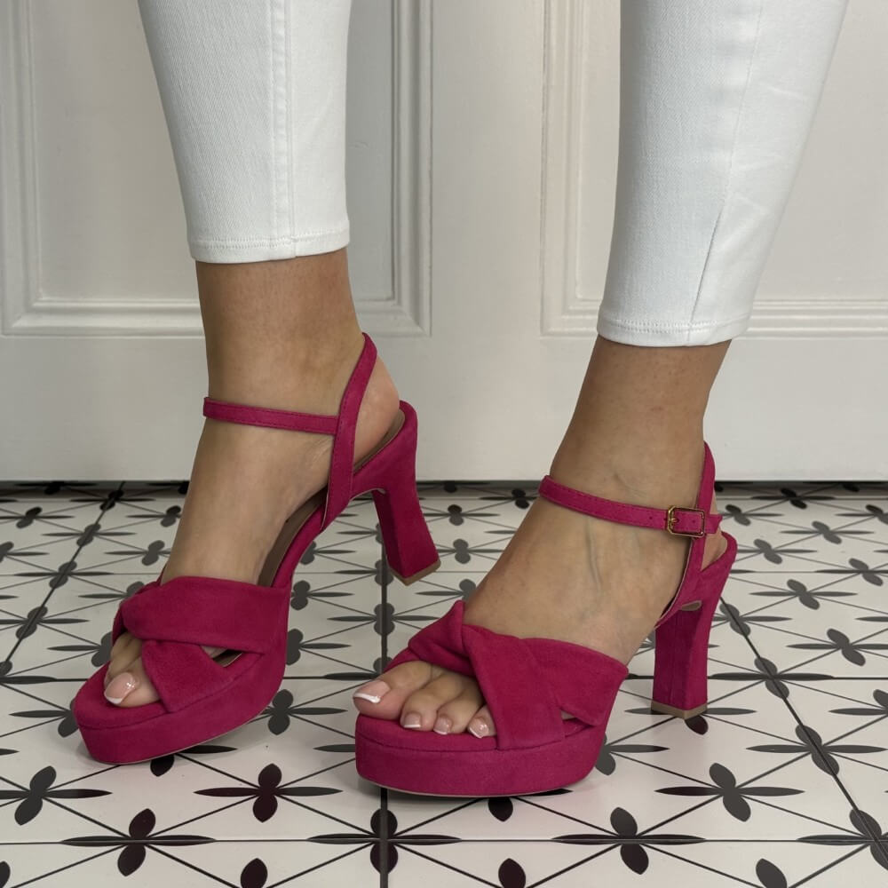 Pink platform sandals worn with white pants on a patterned floor.