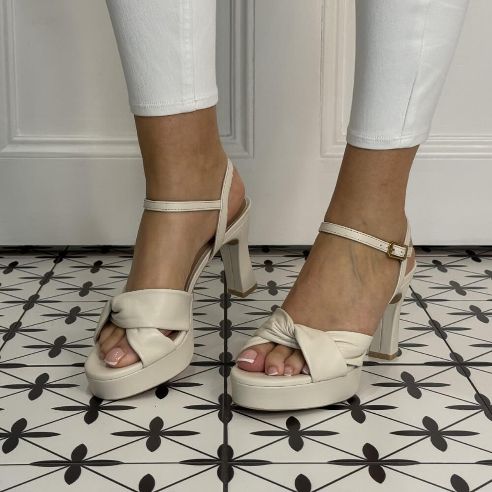Ivory White high-heeled sandals worn with white pants on a patterned floor.