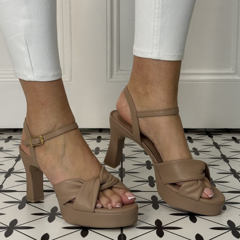 Brown high-heeled sandals worn with white pants on a patterned floor.