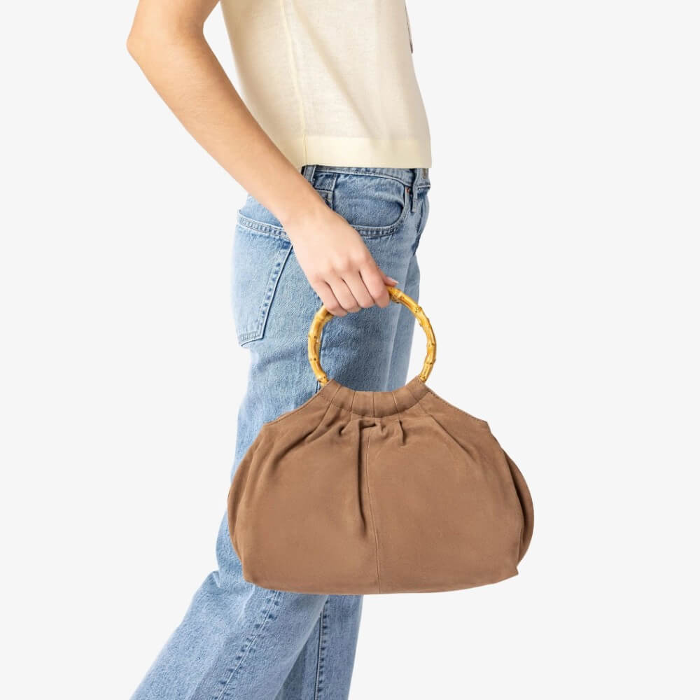 Person holding an Unisa brown handbag with a wooden handle on a white background