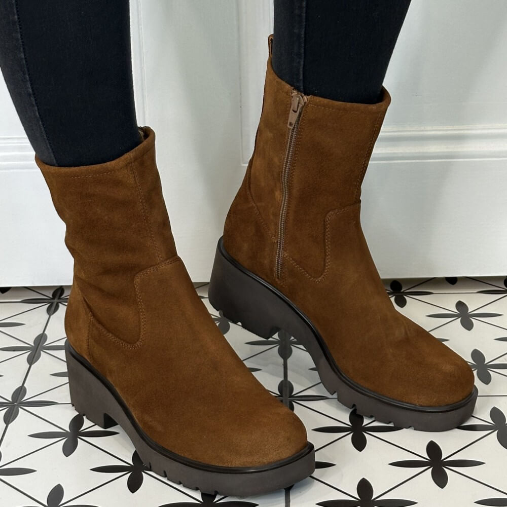 Brown suede ankle boots with black soles on a patterned floor.