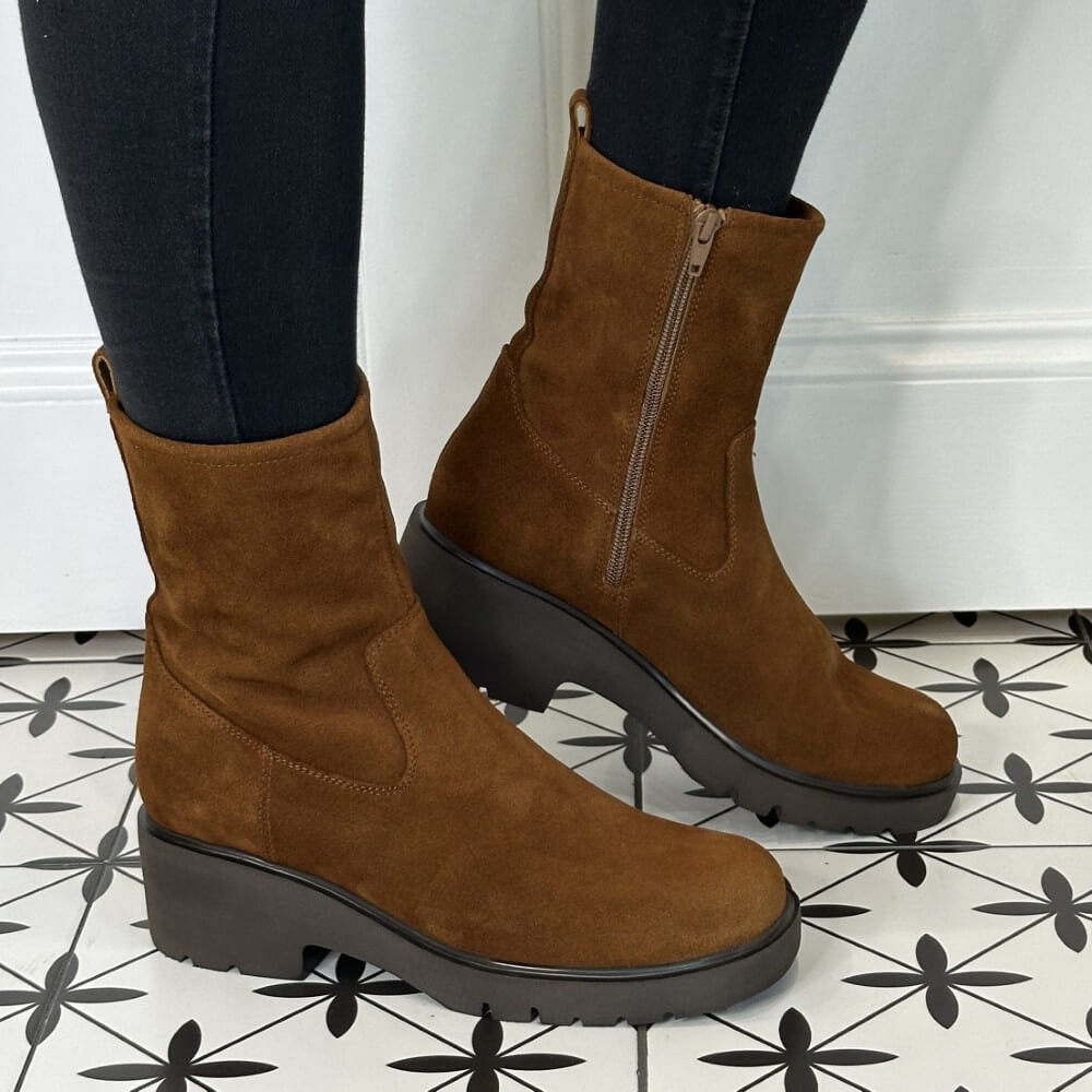 Brown suede ankle boots worn indoors on a patterned floor.