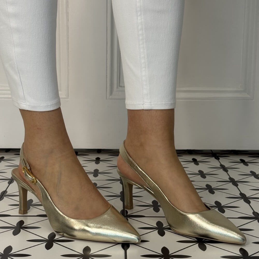 Gold high-heeled shoes worn with white pants on a patterned floor. unisa lanz