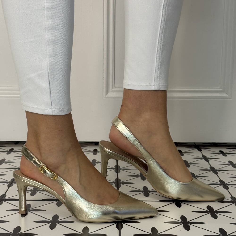 Gold high-heeled shoes worn with white pants on a patterned floor. unisa lanz