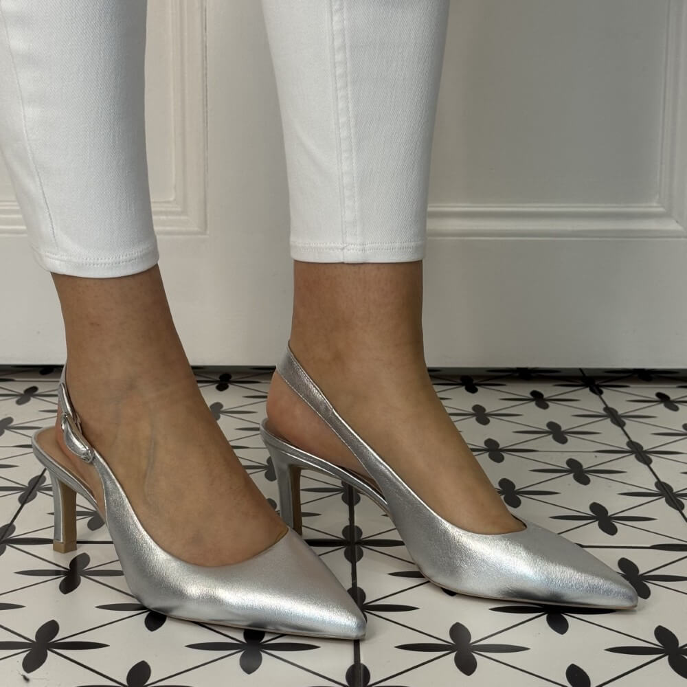 Silver high-heeled shoes worn with white pants on a patterned floor. unisa lanz