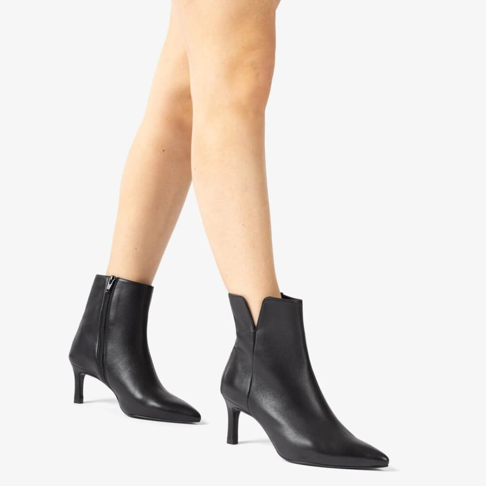 Black high-heeled ankle boots worn by a person on a white background Unisa Loroya Pointed Toe Leather Ankle Boot Black
