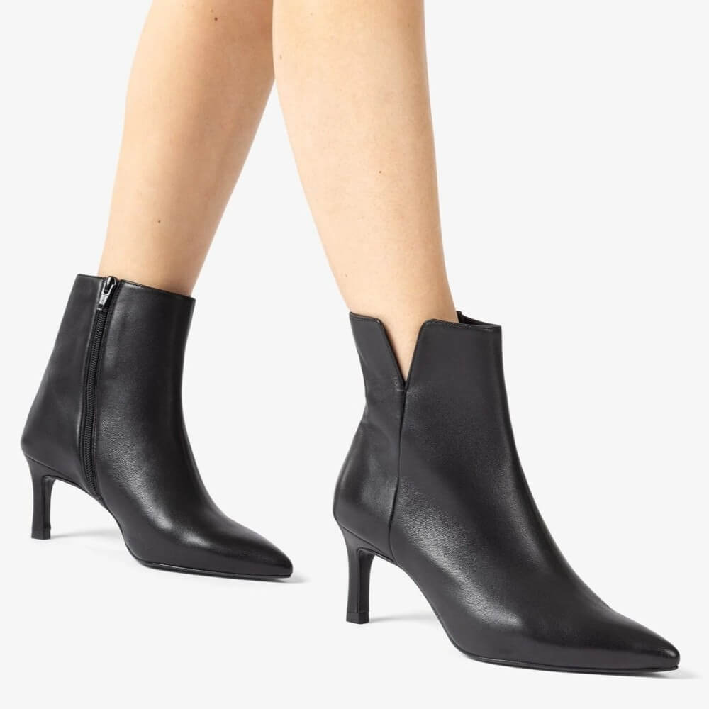 Black ankle boots worn by a person on a light gray background Unisa Loroya Pointed Toe Leather Ankle Boot Black