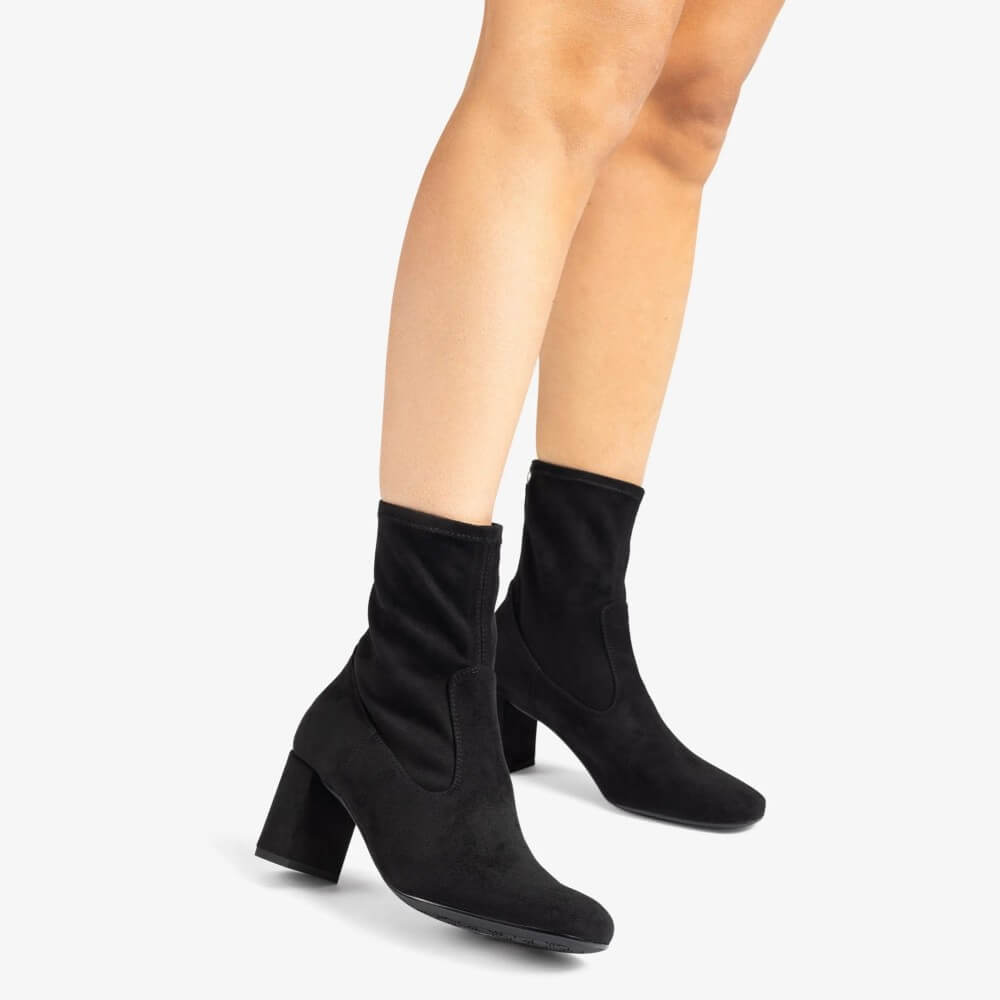 Black ankle boots worn by a person on a white background Unisa Marvy Square toe ankle boot made in faux suede