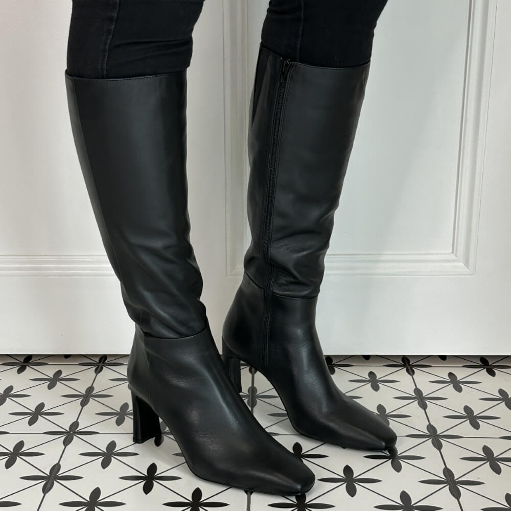 Black knee-high boots on a patterned floor with a white wall background Unisa Wolcot Leather Knee High Boot Black