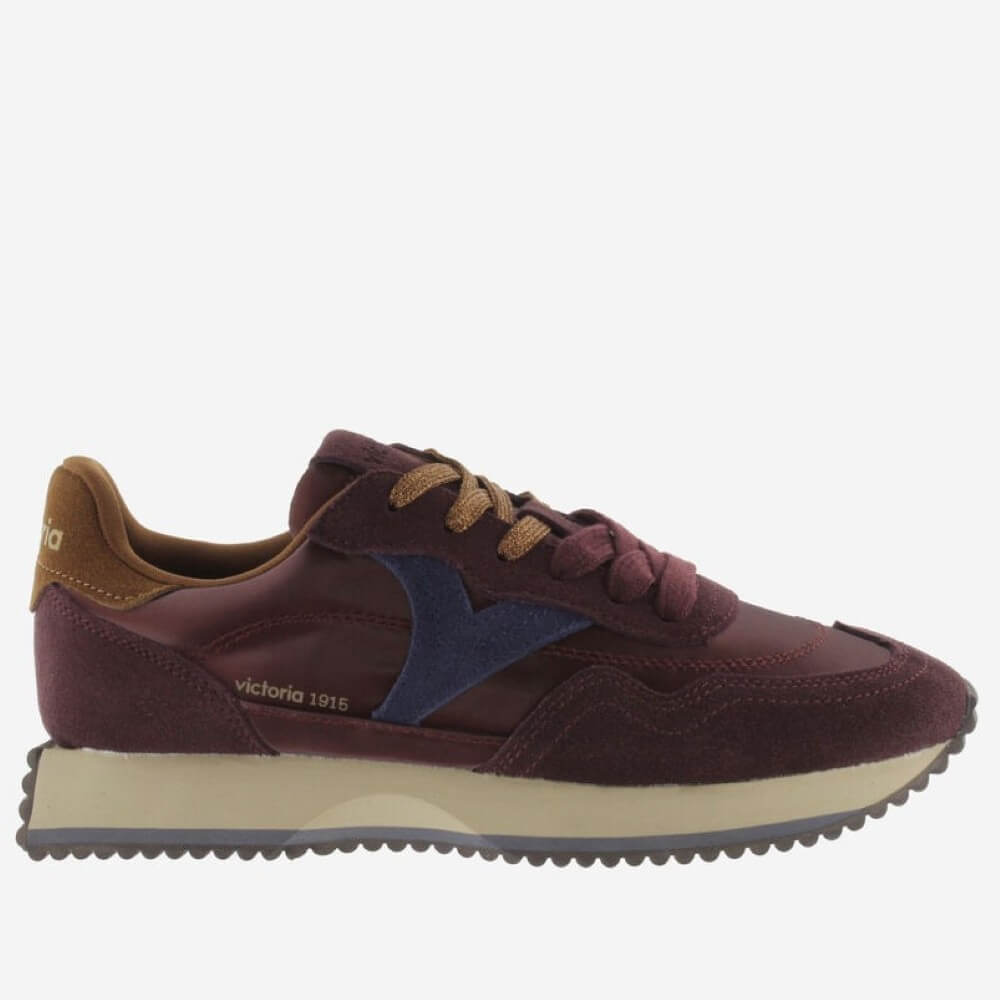 A Victoria low-top suede sneaker in burgundy with a navy blue chevron logo, tan laces, a tan heel tab, and a cream midsole, shown in profile against a light grey background.