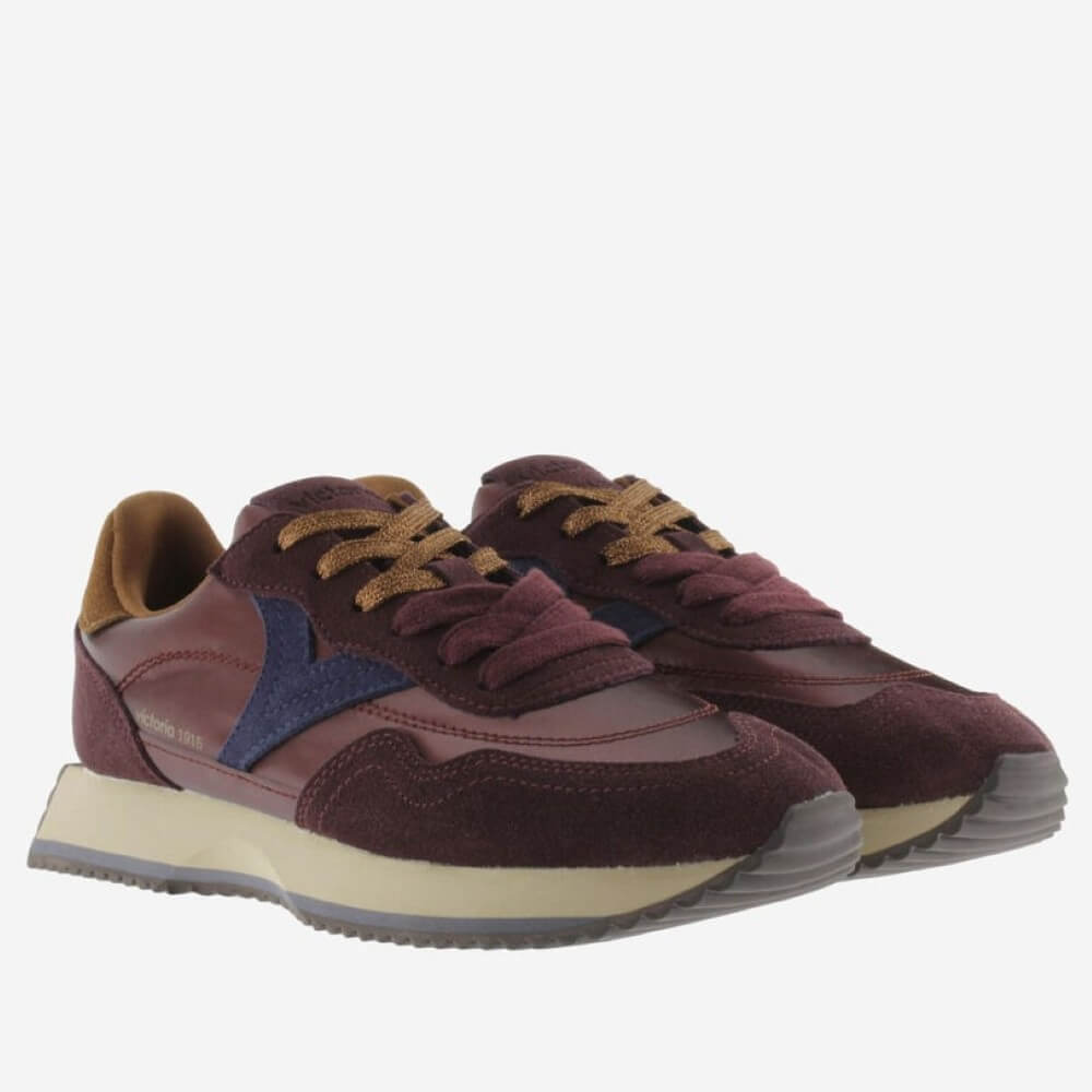 A pair of Victoria vintage-style low-top sneakers in burgundy suede and leather, featuring a navy blue chevron logo, tan laces, a cream midsole, and a grey outsole, shown against a plain light grey background.