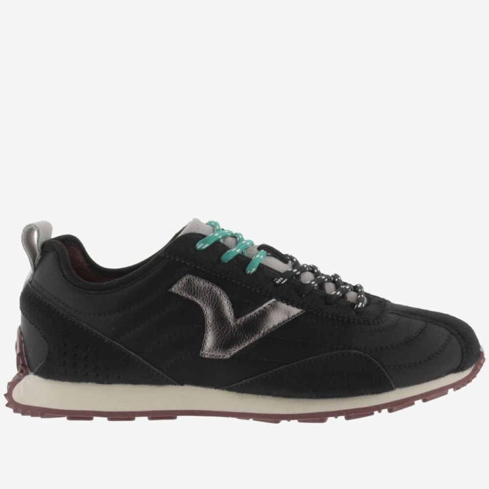 A black Victoria sneaker with a metallic silver V logo on the side, teal laces, and a cream midsole, shown against a light grey background.
