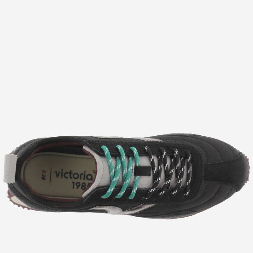 A black Victoria sneaker with a metallic silver V logo on the side, teal laces, and a cream midsole, shown against a light grey background.
