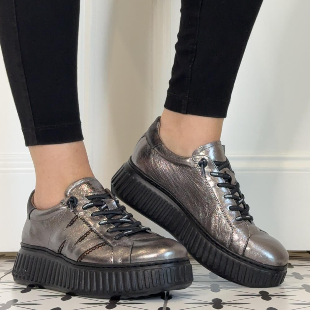 Wonders Metallic silver low-top platform sneakers with black elastic laces and chunky black soles, shown on a person wearing black leggings.