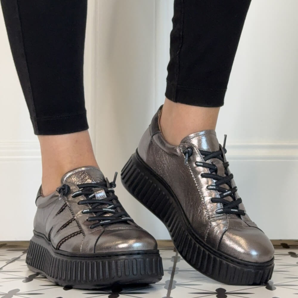 Wonders Metallic silver low-top platform sneakers with black elastic laces and chunky black soles, shown on a person wearing black leggings.