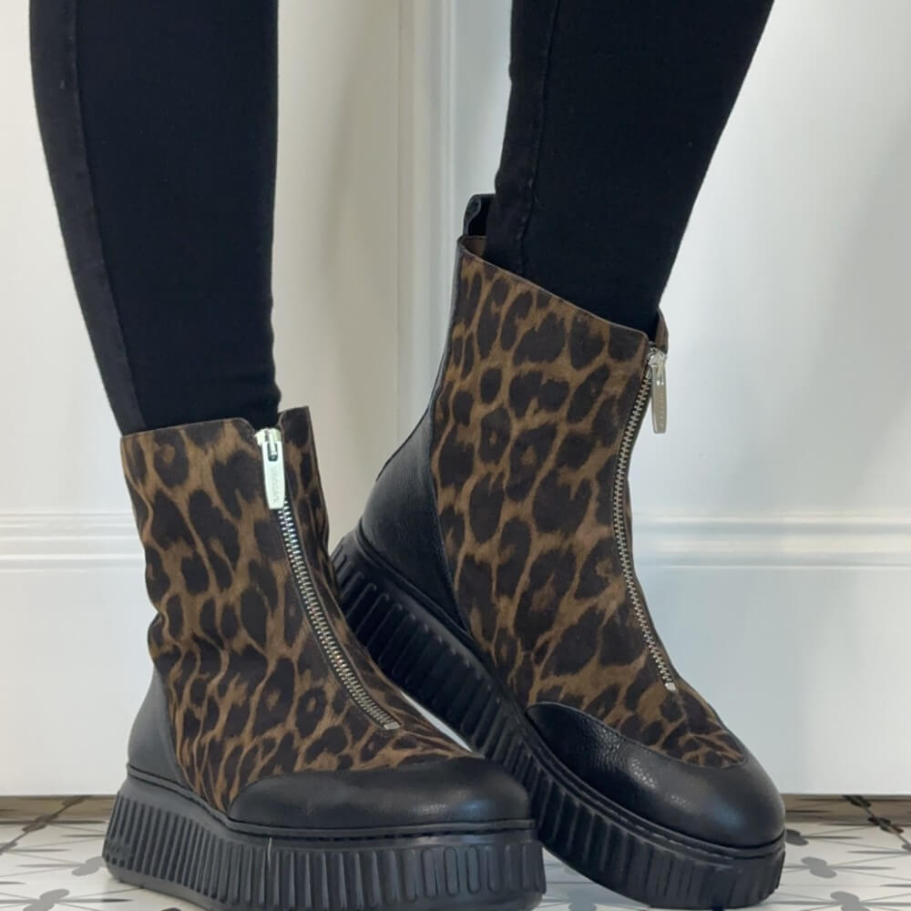 A pair of Wonders ankle boots with a leopard print pattern on the uppers and black leather side panels, worn with black leggings. The boots feature a chunky black platform sole and a front zipper.