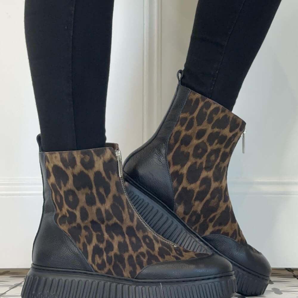 A pair of Wonders ankle boots with a leopard print pattern on the uppers and black leather side panels, worn with black leggings. The boots feature a chunky black platform sole and a front zipper.