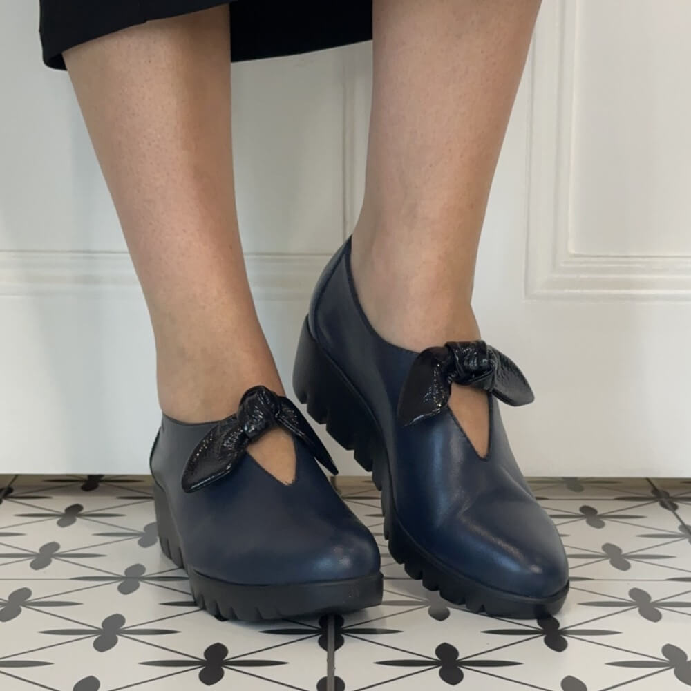 Wonders navy leather slip-on with a patent bow trim and a black wedge sole worn on a tiled floor