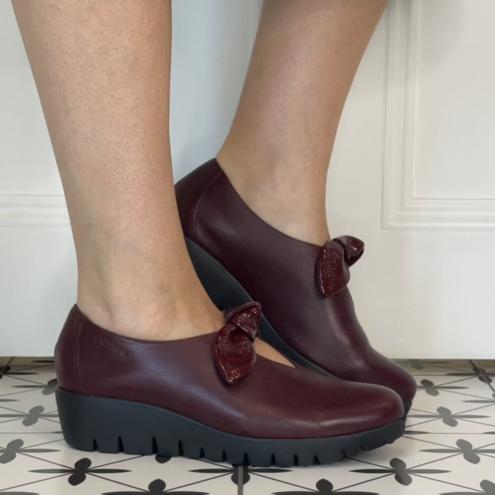Wonders Wine leather slip-on with a patent bow trim and a black wedge sole worn on a tiled floor
