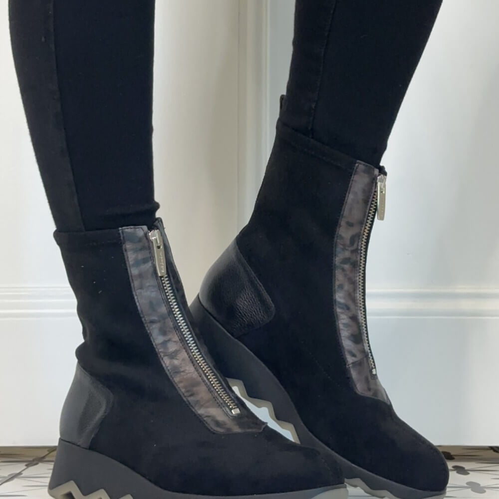  Wonders Black ankle boots with front zippers and textured side panels, worn with black leggings against a white wall.