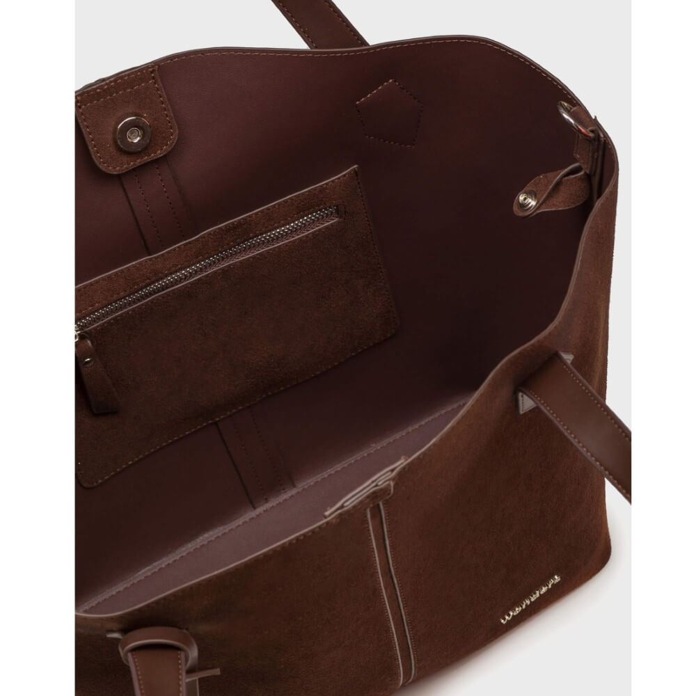 Close-up of the interior of a dark brown leather tote bag, showing a zippered pocket, interior lining, and a small gold-toned logo near the bottom right corner.