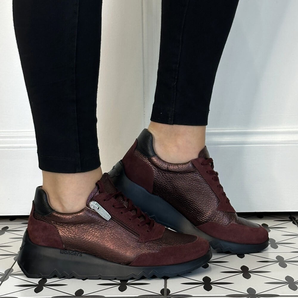 A person wearing Wonders burgundy and black platform sneakers with black leggings, standing on a black and white patterned tile floor in front of a white wall.