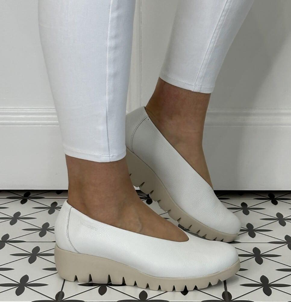 White flat shoes worn with white pants on a patterned floor.