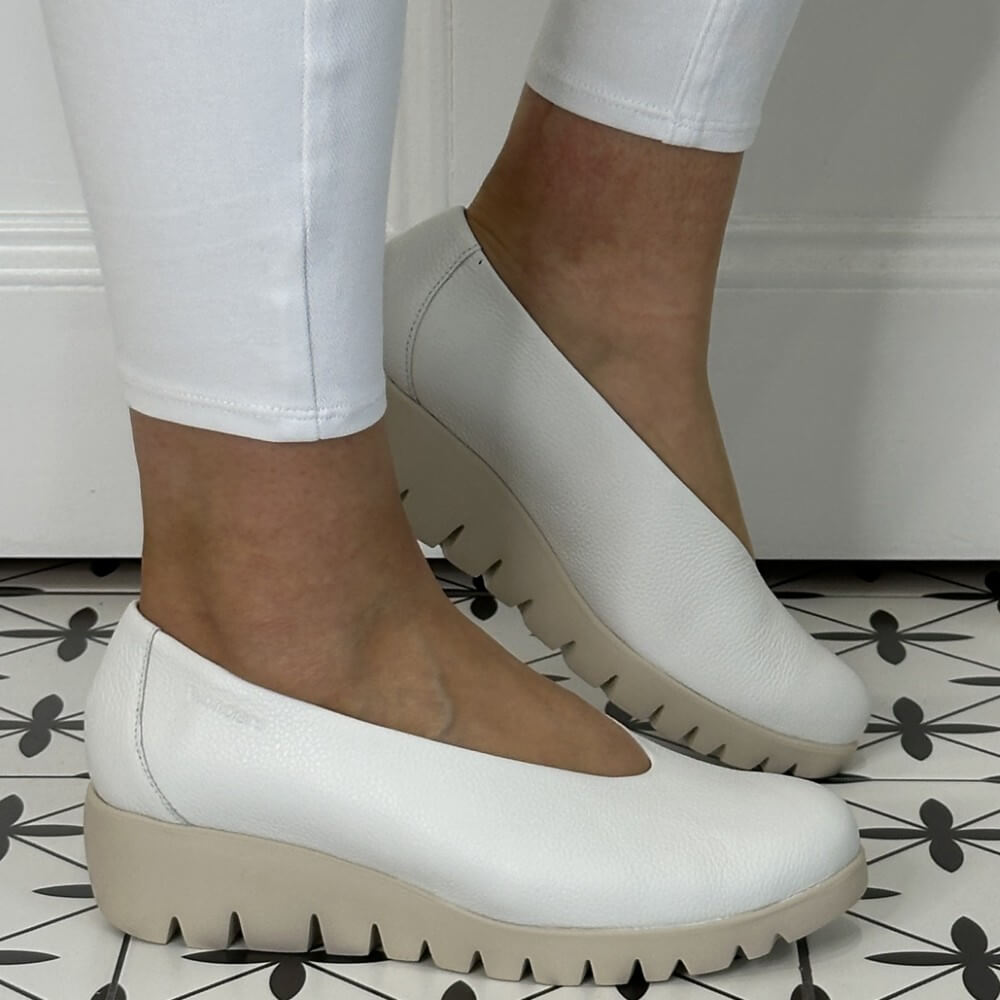 White platform shoes worn with white pants on a black and white patterned floor.