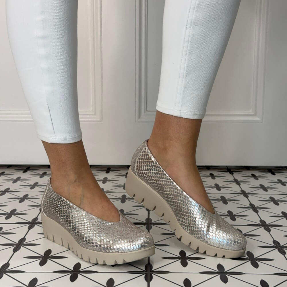 gold wedge shoes worn with white pants on a patterned floor.