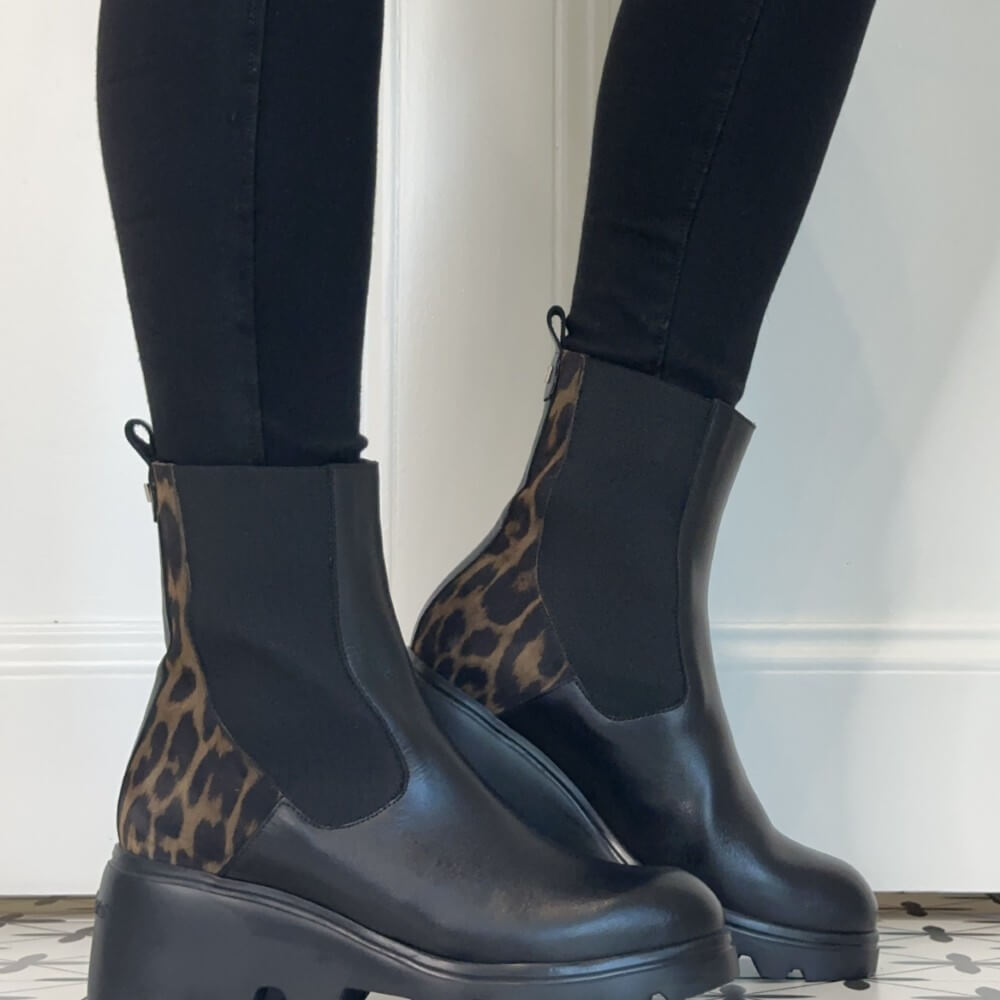 Wonders Black leather Chelsea-style ankle boots with leopard-print fabric panels on the heel and back, worn with black leggings.