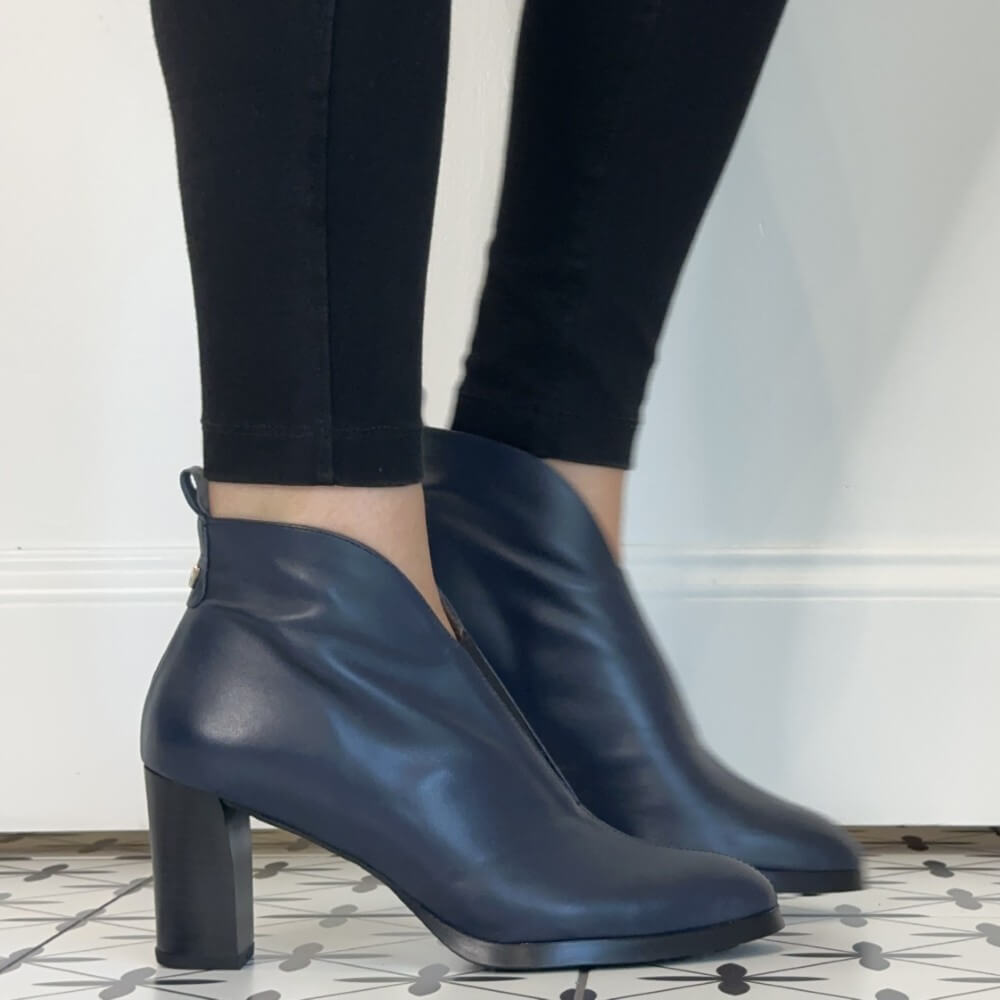 A pair of Wonders dark navy blue leather ankle boots with block heels, worn with black leggings on a patterned tile floor against a white wall.