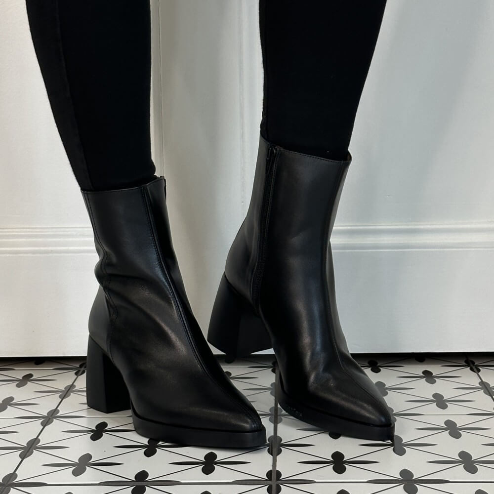 Wonders Black leather ankle boots with block heels and side zippers, shown on a model wearing black leggings on a black and white patterned tile floor.