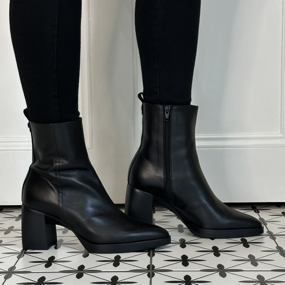 Wonders Black leather ankle boots with block heels and side zippers, shown on a model wearing black leggings on a black and white patterned tile floor.