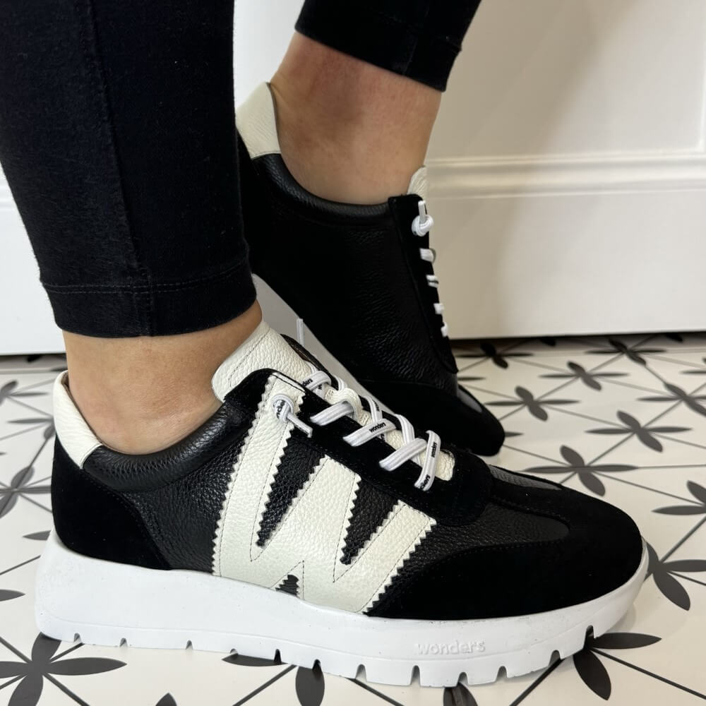 Black and white sneakers worn indoors on a patterned floor.