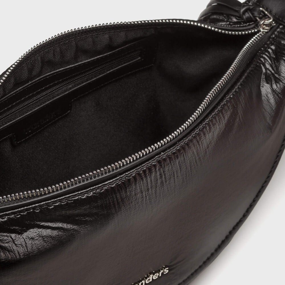 Close-up of an open black fabric pouch or clutch with silver-tone zipper hardware, showing the interior lining and a small brand mark near the bottom edge.