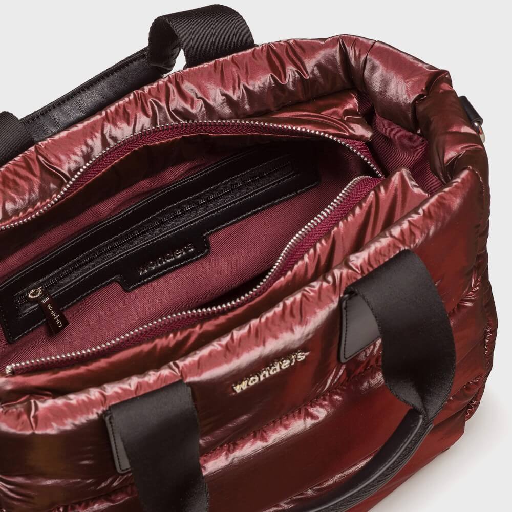 Close-up of the interior of a shiny burgundy puffer bag with black handles and a zippered compartment. The brand name 'Wonders' is visible on the interior label and zipper pull.