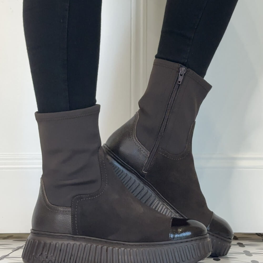  A pair of Wonders dark brown ankle boots with elastic side panels, chunky lug soles, and glossy patent leather toe caps, shown on a model wearing black leggings.