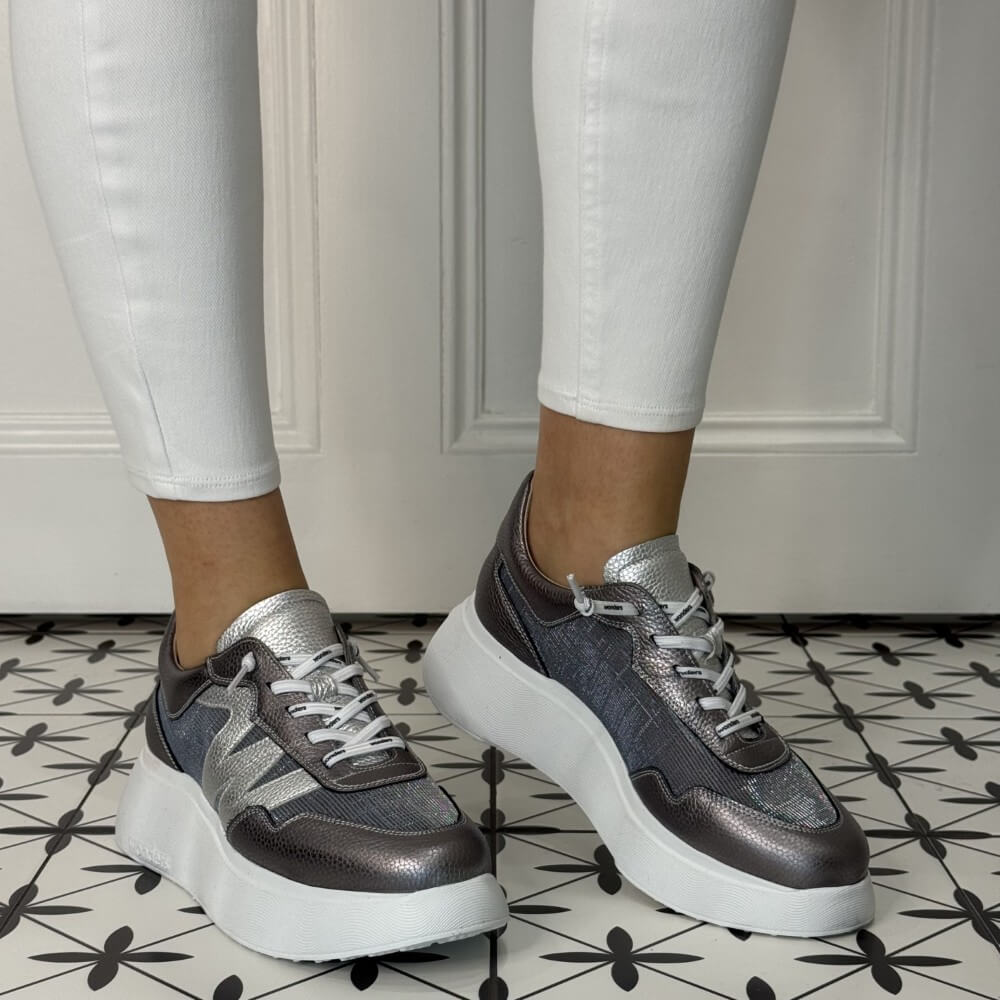 Grey sneakers with white soles worn by a person on a patterned floor. Wonders