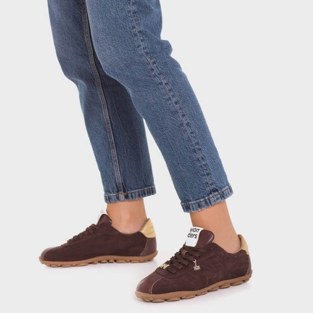 Brown sneakers worn with blue jeans on a white background